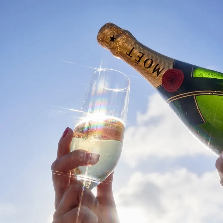 sparkling champagne flute with an unopened bottle of Moet champagne against a backdrop of fluffy clouds